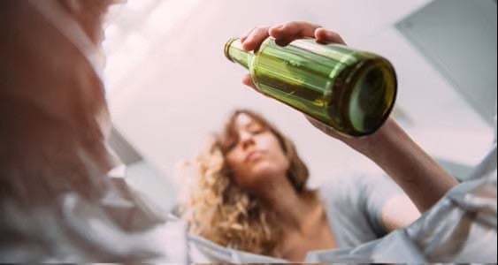 Una imagen de una mujer bebiendo de una botella de cerveza verde. Se ve desenfocada, desde una perspectiva baja.